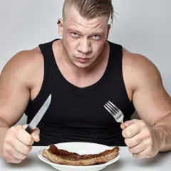 Mężczyzna z widoczną muskulaturą, z determinacją wpatruje się w stek na talerzu. To jego sposób na to, jak przytyć.