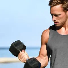 Mężczyzna ćwiczy biceps na plaży, wykonując kolejne powtórzenia z hantlem.