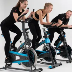 Trzy osoby ćwiczą na rowerach stacjonarnych. Wesoła atmosfera podczas treningu spinningowego.