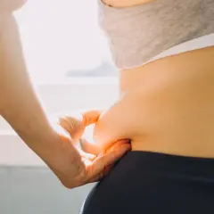 Dłoń chwyta fałd skóry na boku, symbolizując troskę o sylwetkę i chęć poznania, jak przyspieszyć metabolizm.
