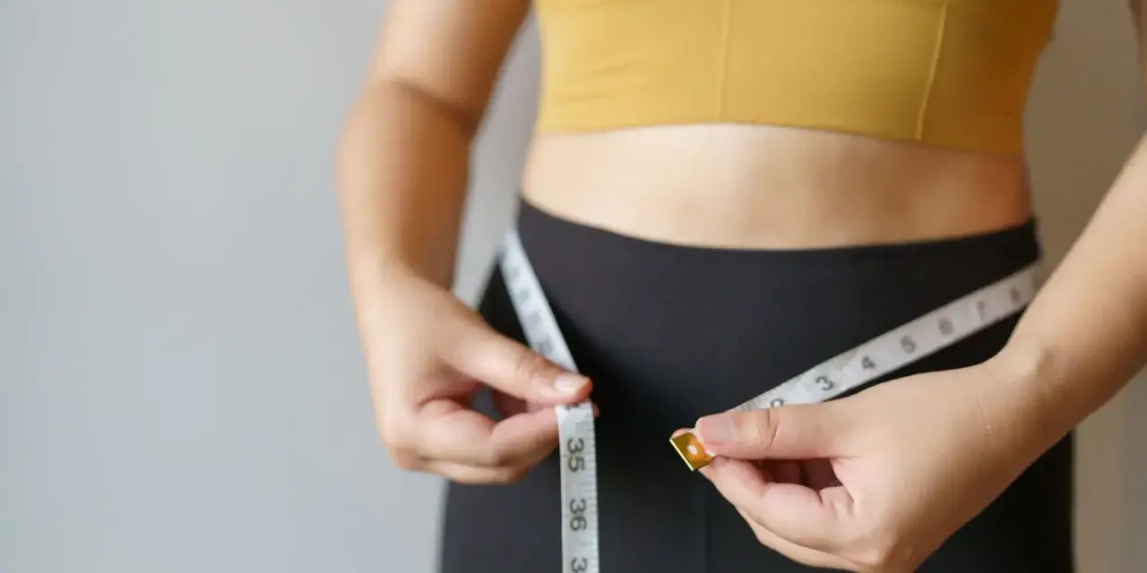 Kobieta mierzy talię centymetrem. Chcesz wiedzieć, jak podkręcić metabolizm po 40.? To pierwszy krok do celu.